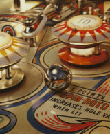 A pinball detail with red and yellow bumpers and a chrome-plated ball