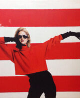 Blonde woman in a red and black outfit in front of a red-striped wall